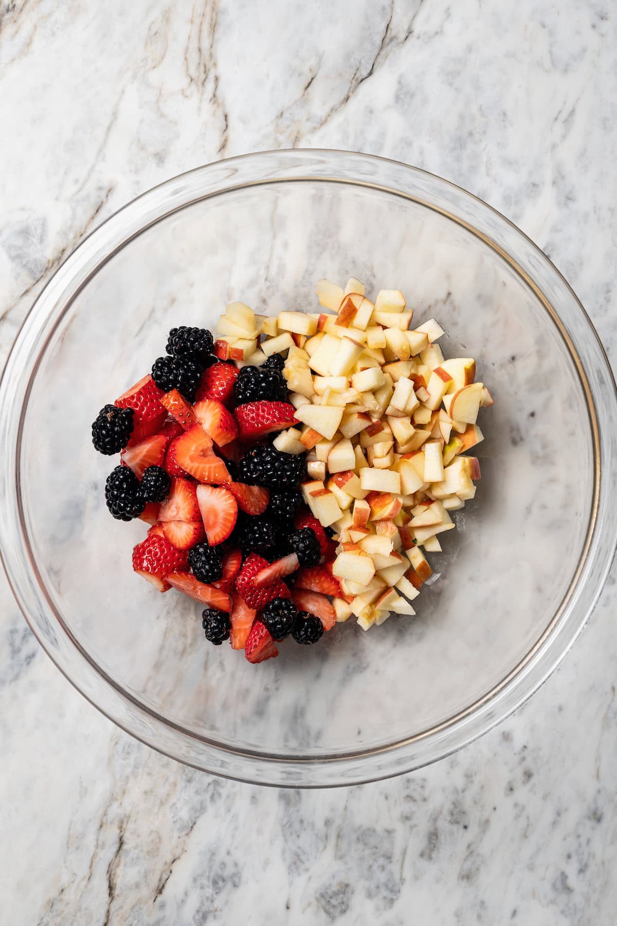 This easy mixed berry pie recipe combines three types of juicy berries with tender apples inside a light and flaky homemade pie crust. Diced apples and mixed berries added to a bowl.