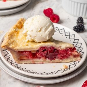 A slice of berry pie topped with a scoop of ice cream on a plate.