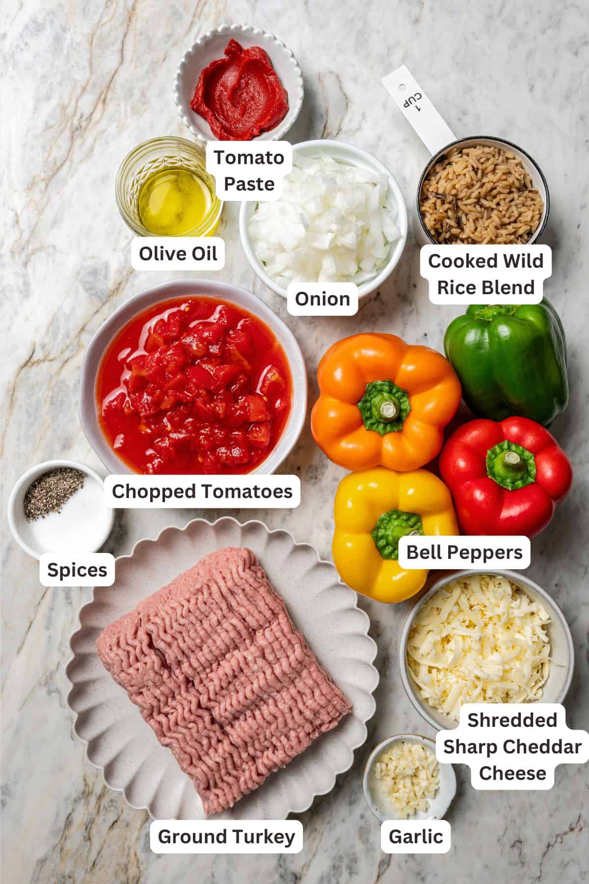 Esses pimentões recheados de peru moídos clássicos estão repletos de carne moída temperada, arroz selvagem e tomate suculento, coberto com queijo derretido e assado. Os ingredientes do pimentão recheado de peru moídos com rótulos de texto sobrepostos a cada ingrediente.