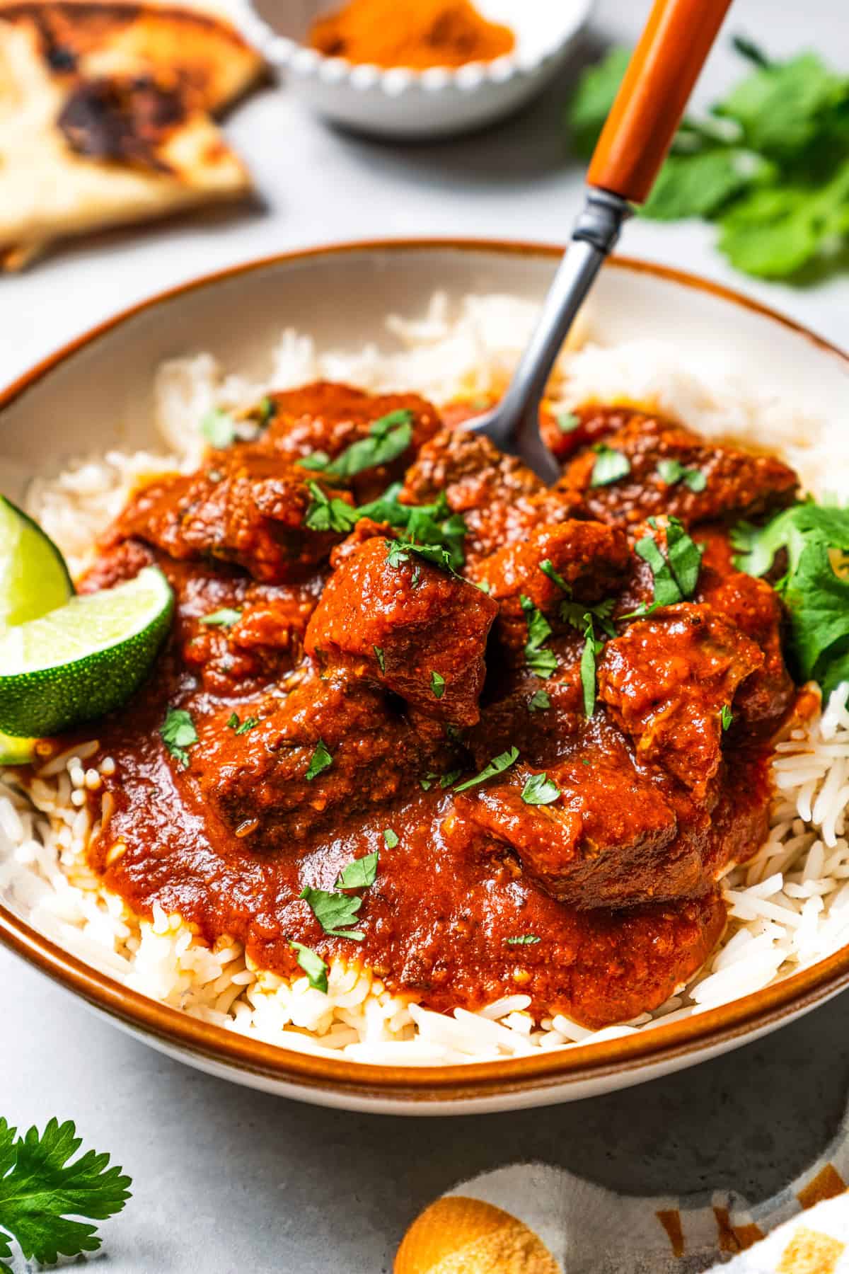 A fork in a bowl of beef madras curry served over rice.