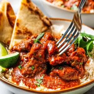 Beef madras curry served over a bowl of rice with a side of naan bread.