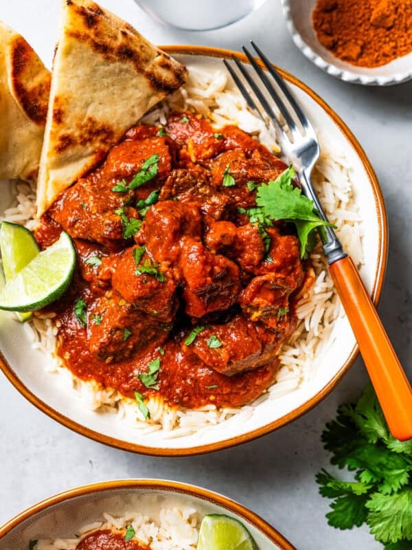 Beef Madras Curry served over a bowl of rice with naan bread, with a fork.