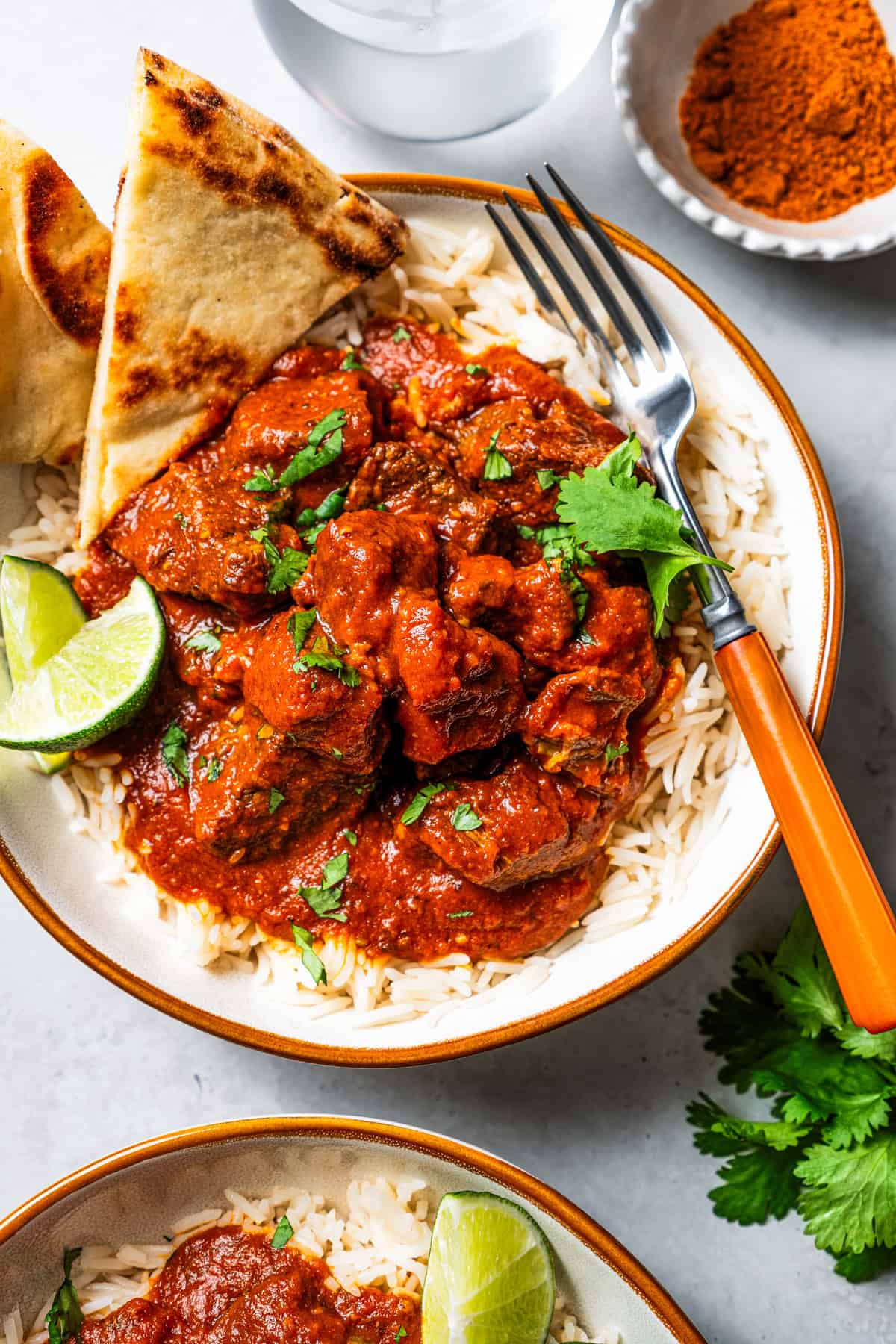 This beef madras is an easy curry recipe with tender beef simmered in a rich, spiced tomato onion gravy. Serve it with naan bread and rice. Beef Madras Curry served over a bowl of rice with naan bread, with a fork.