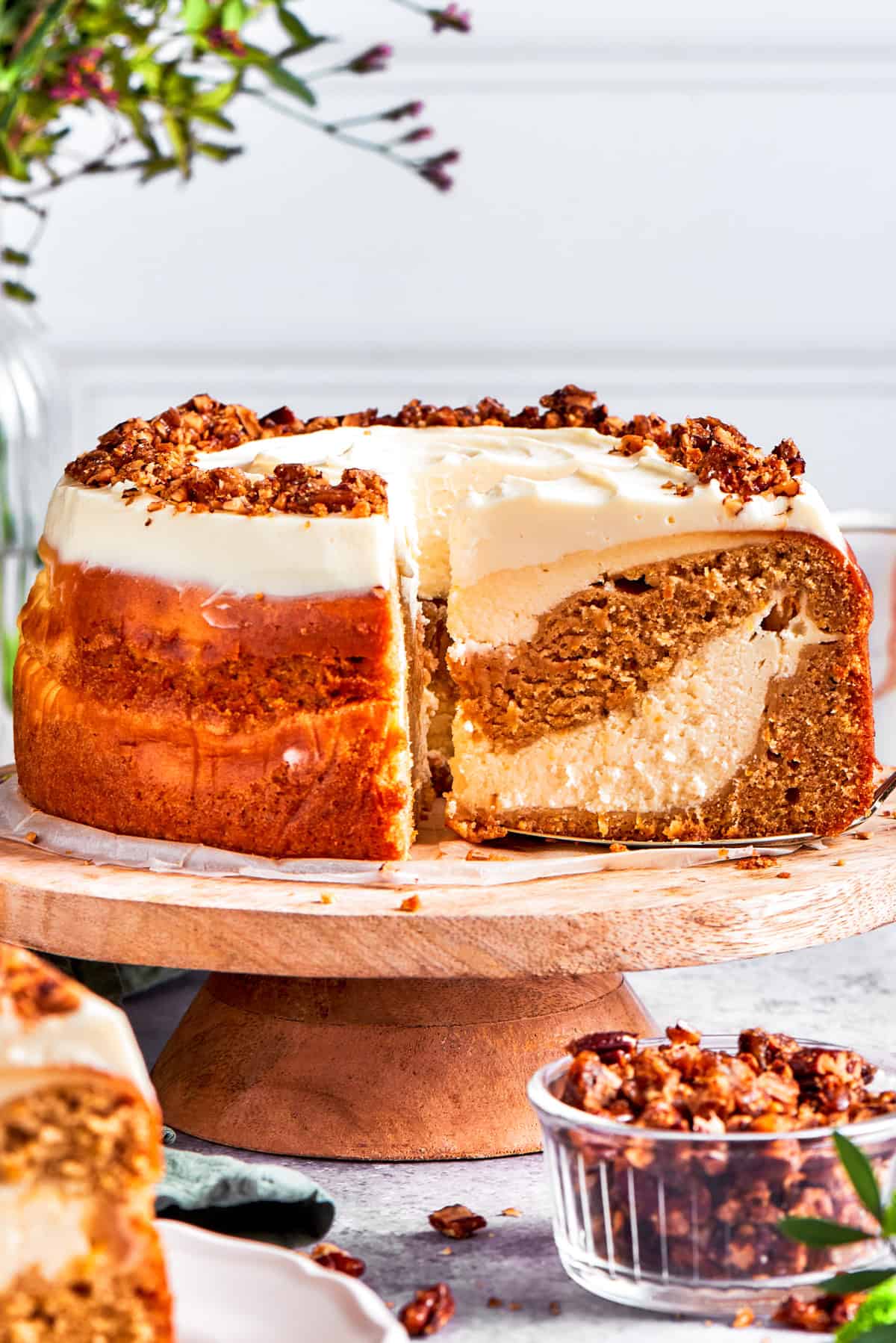 Carrot Cake Cheesecake Recipe Carrot cake cheesecake on a cake stand with a slice pulled out to see the interior.