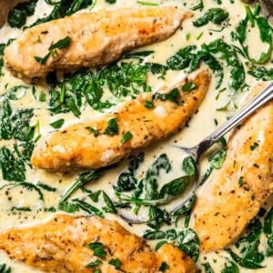 Overhead view of a spoon resting in chicken Florentine in a skillet with spinach cream sauce.