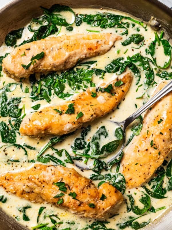 Overhead view of a spoon resting in chicken Florentine in a skillet with spinach cream sauce.