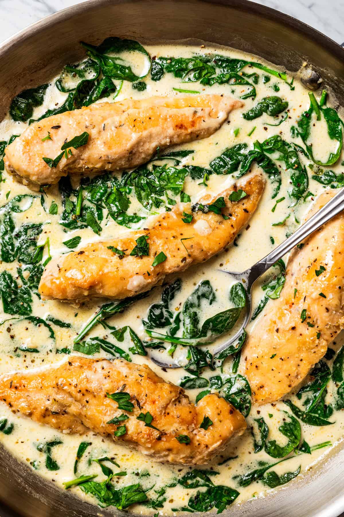 Creamy chicken Florentine is a one-pan dinner with golden-fried chicken smothered in a garlicky spinach cream sauce. Make it in 30 minutes! Overhead view of a spoon resting in chicken Florentine in a skillet with spinach cream sauce.