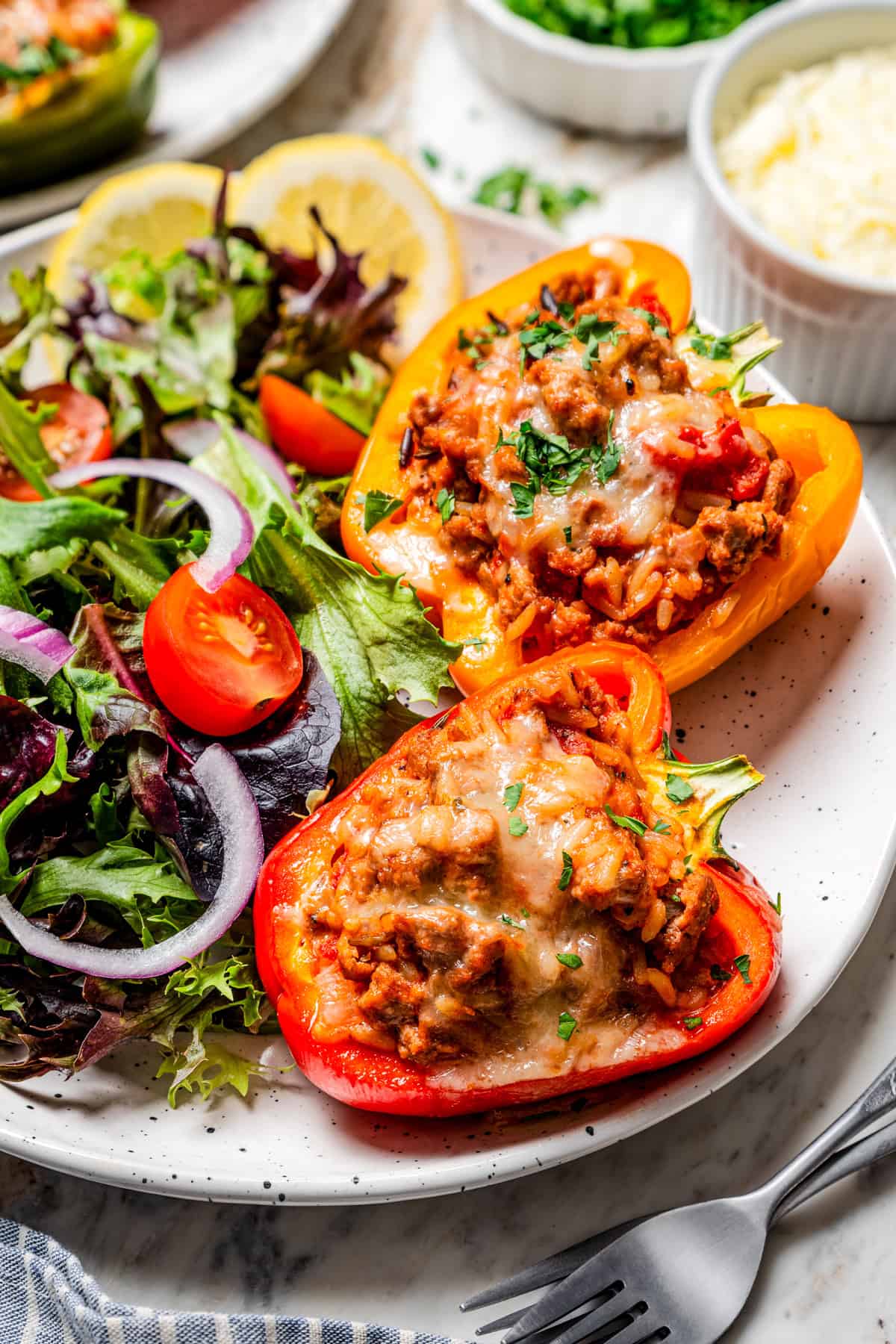 These classic ground turkey stuffed peppers are packed with seasoned ground meat, wild rice, and juicy tomatoes, topped with melty cheese and baked. Two ground turkey stuffed peppers next to a side of green salad on a plate.