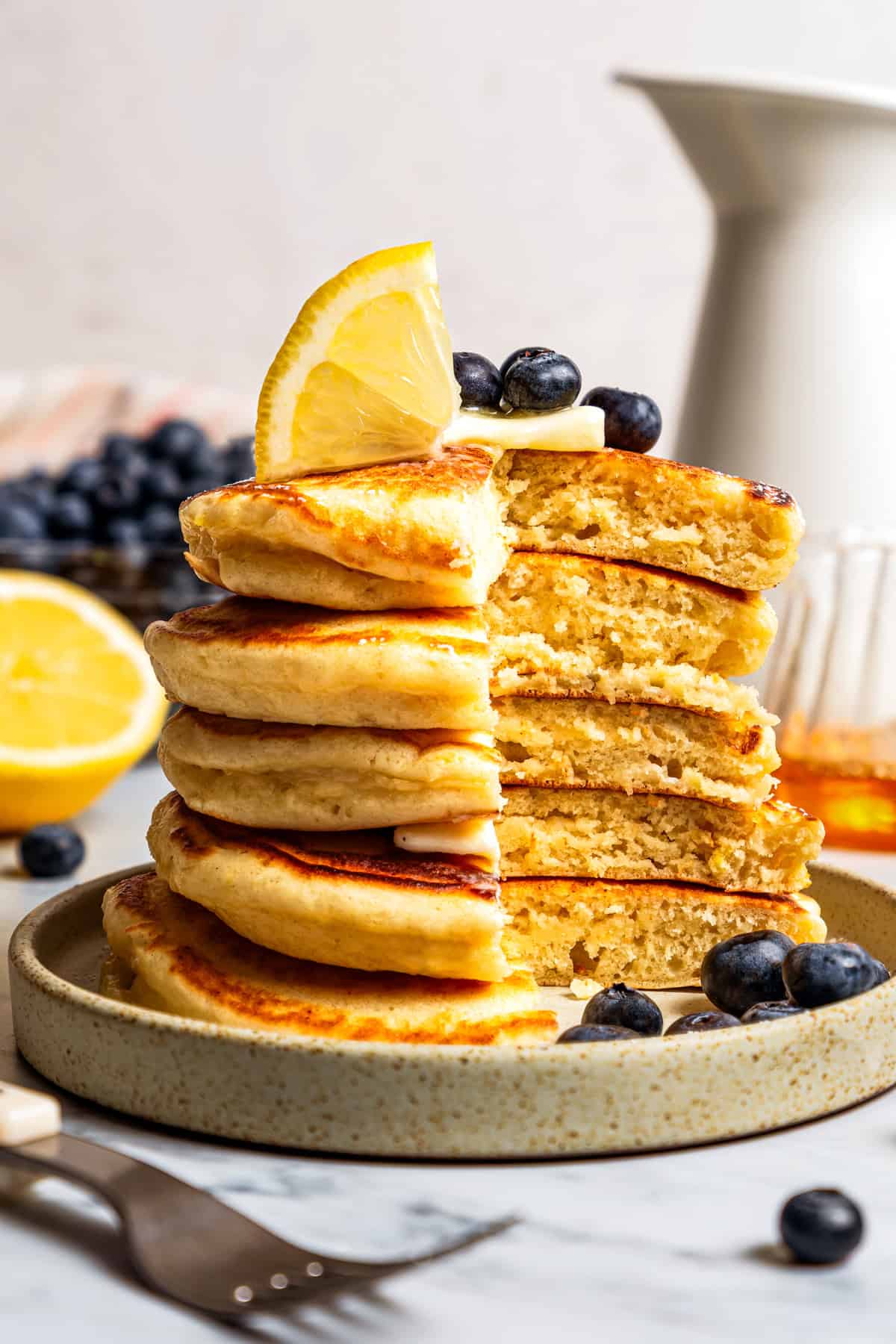 Side view of a stack of lemon ricotta pancakes on a stoneware plate with a large slice missing from the stack.