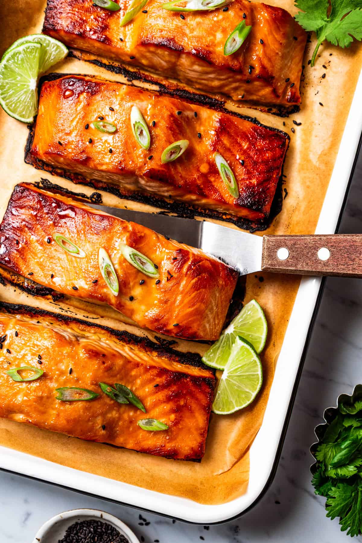 This sweet and savory miso salmon is caramelized outside and tender and flaky inside. Serve it with rice for a quick, easy salmon dinner! Miso salmon on a lined baking tray, with a spatula tucked under one of the fillets.