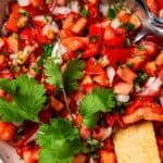 Overhead view of a tortilla chip resting in a bowl of pico de gallo.