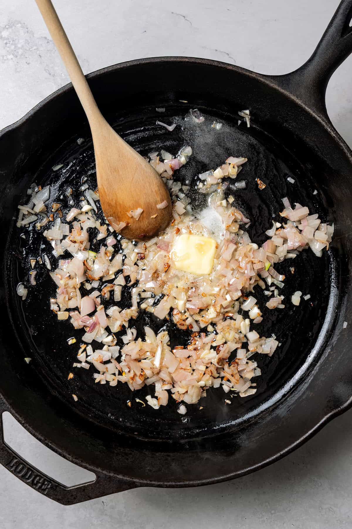 This easy homemade arancini recipe makes crispy, cheesy, golden-fried Italian rice balls filled with melty pockets of tangy goat cheese. Onions sautéing in butter in a skillet with a wooden spoon.