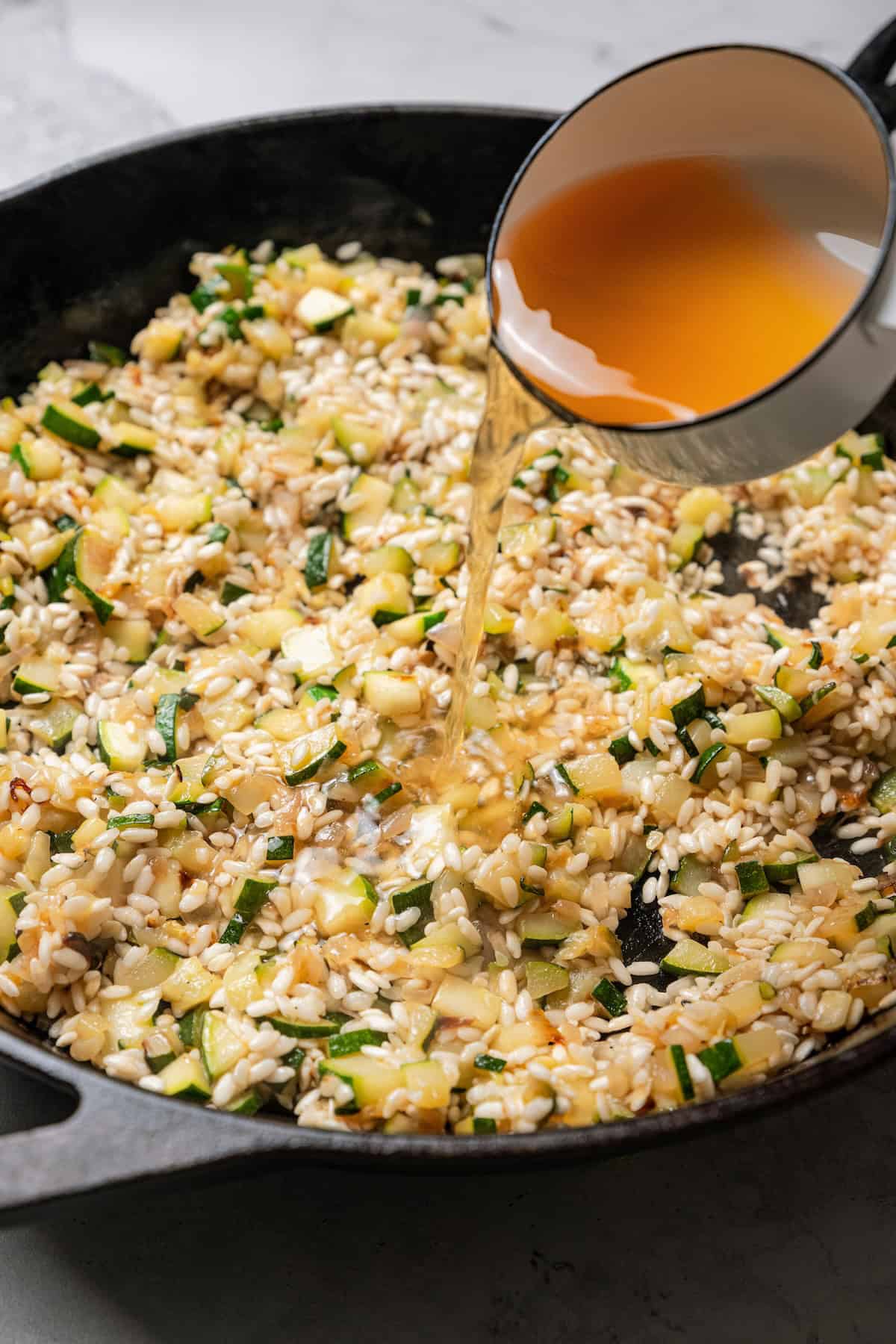 This easy homemade arancini recipe makes crispy, cheesy, golden-fried Italian rice balls filled with melty pockets of tangy goat cheese. Broth being poured into a pan of risotto.