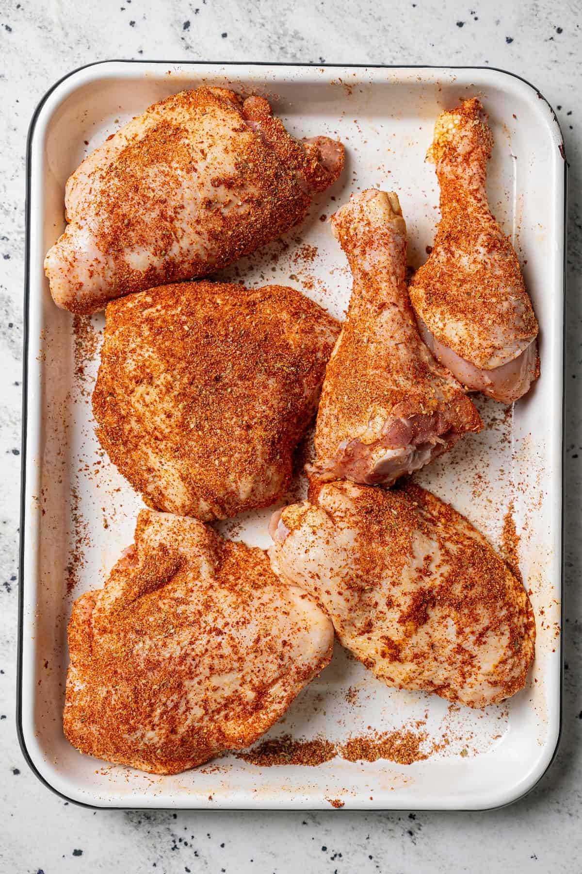 Classic arroz con pollo is a Latin favorite with juicy, seasoned chicken and rice brimming with smoky, savory flavor. Make it in one pot! Seasoned chicken pieces on a baking tray.