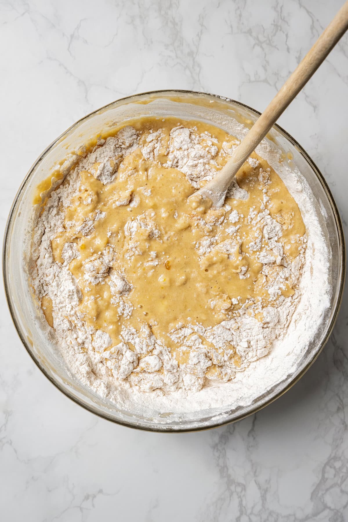 These soft, buttery banana bread muffins are easy to make with maple syrup, brown sugar, and cinnamon. It's impossible to eat just one! Wet and dry muffin batter ingredients combined in a bowl with a wooden spoon.