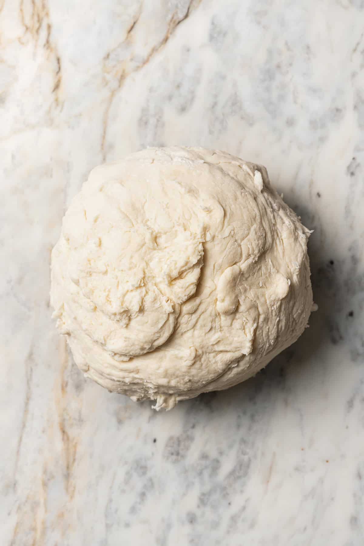 This is the best cherry pie recipe with thick, juicy cherry pie filling flavored with a touch of almond, baked in a buttery, flaky pie crust. A ball of pie dough on a floured countertop.