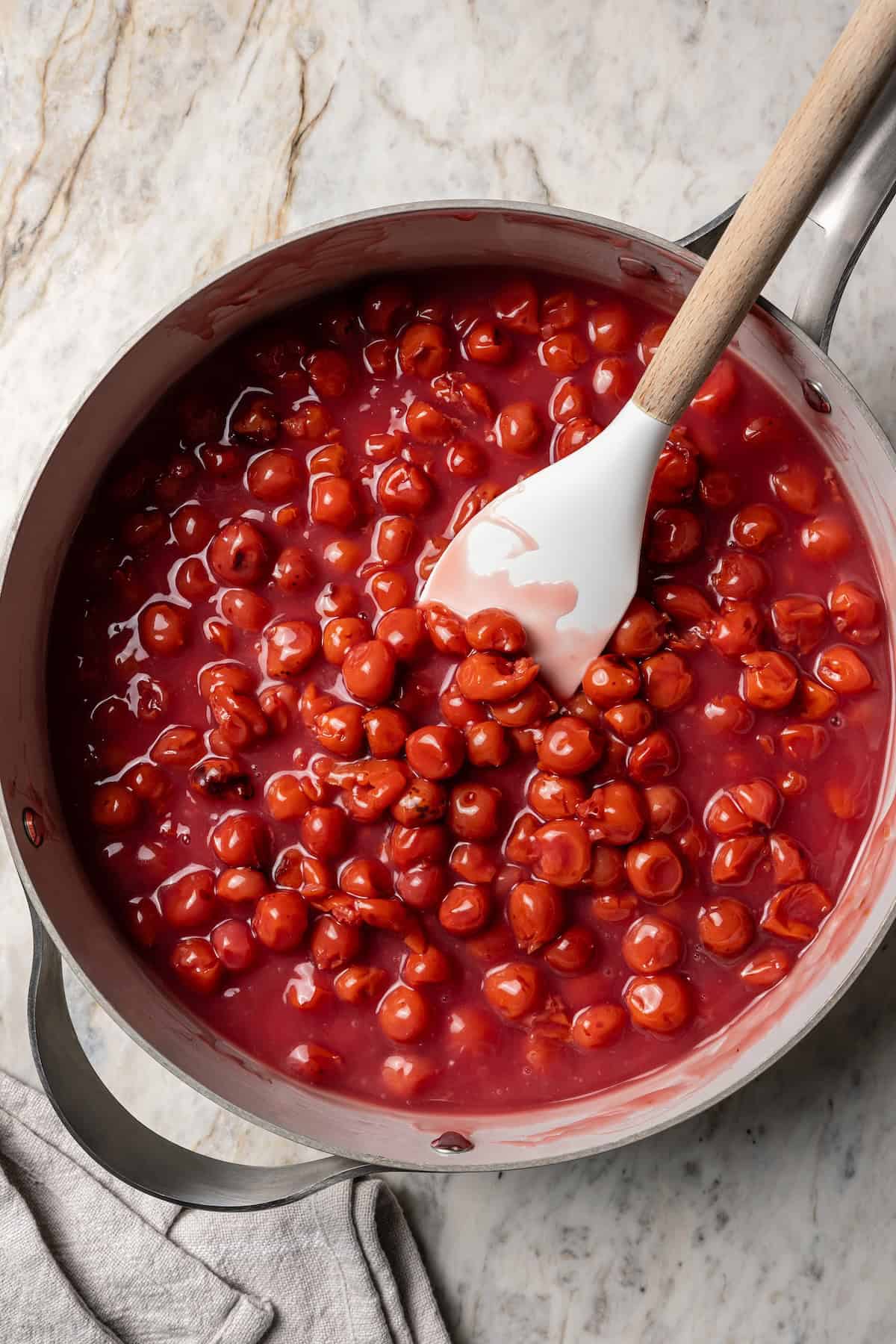 This is the best cherry pie recipe with thick, juicy cherry pie filling flavored with a touch of almond, baked in a buttery, flaky pie crust. Cherry pie filling in a saucepan with a spoon.