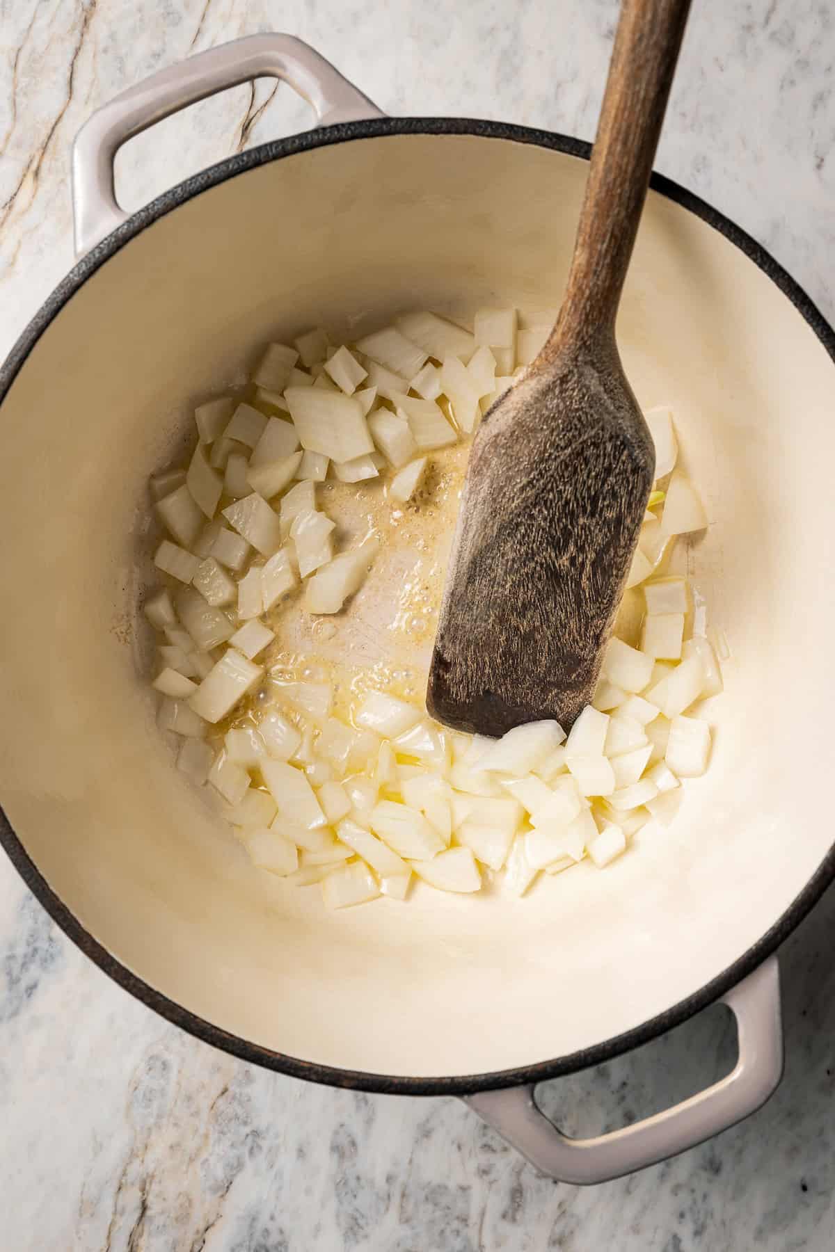 Diced onion sautéing in a pot with a wooden spatula.