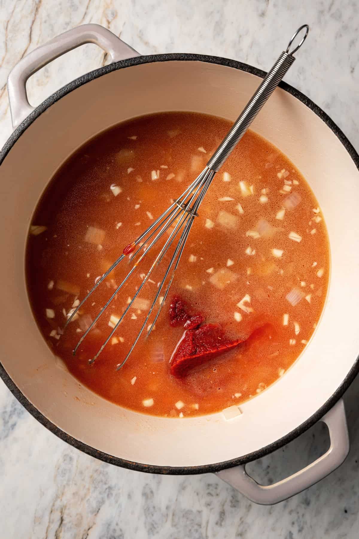 Tomato soup ingredients combined in a pot with a whisk.