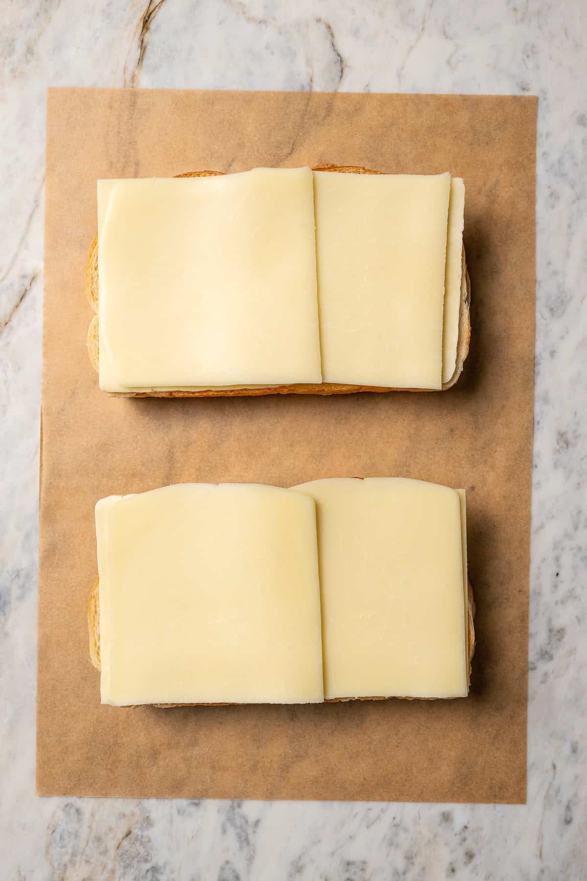 Cheese slices layered over sourdough bread on a piece of parchment paper.