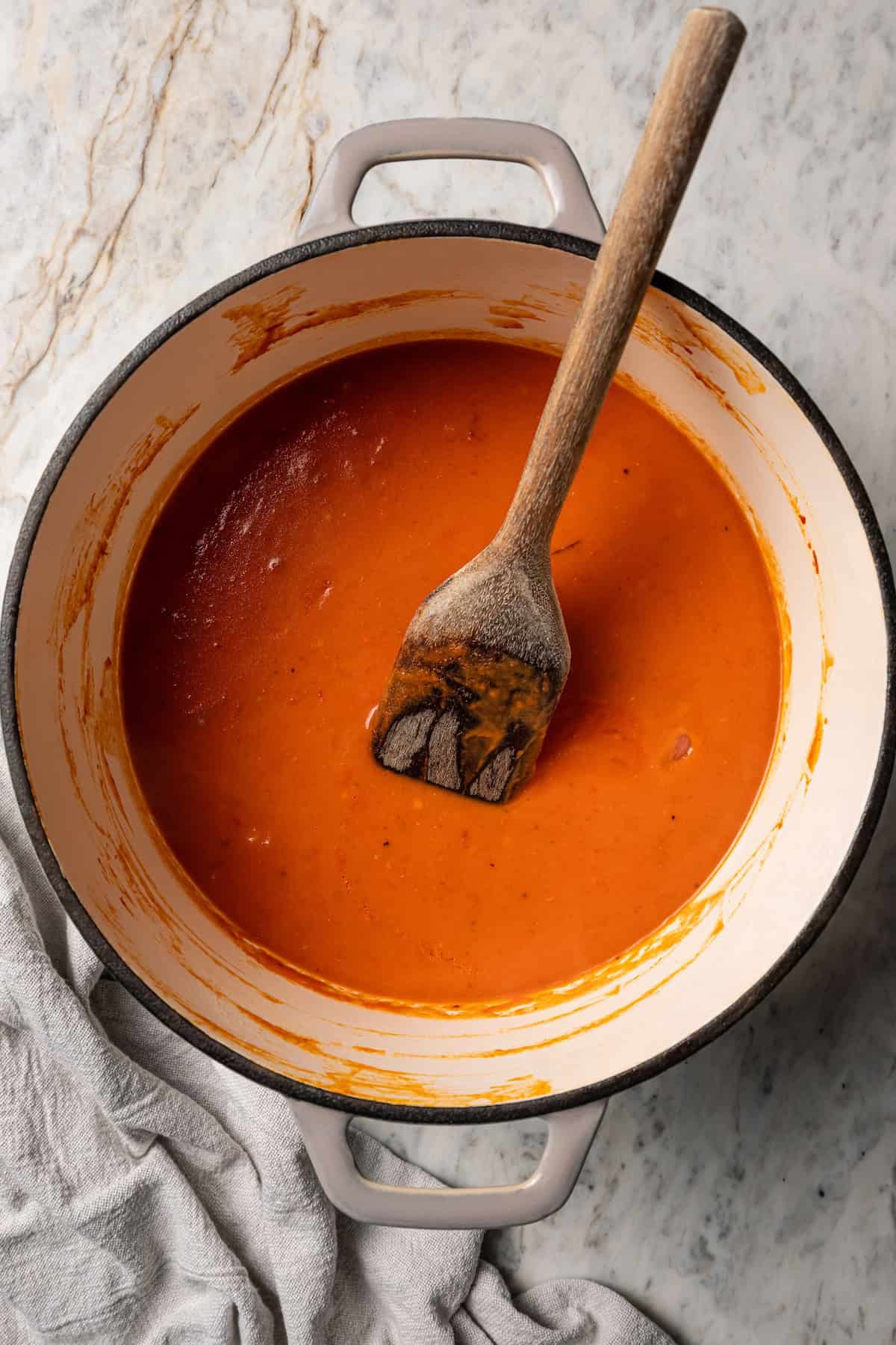 Tomato soup inside a large pot with a wooden spatula.