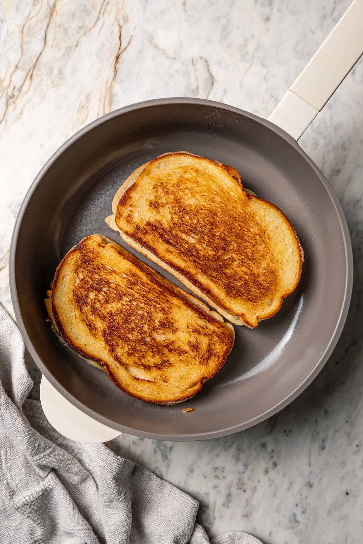 Two grilled cheese sandwiches in a skillet.