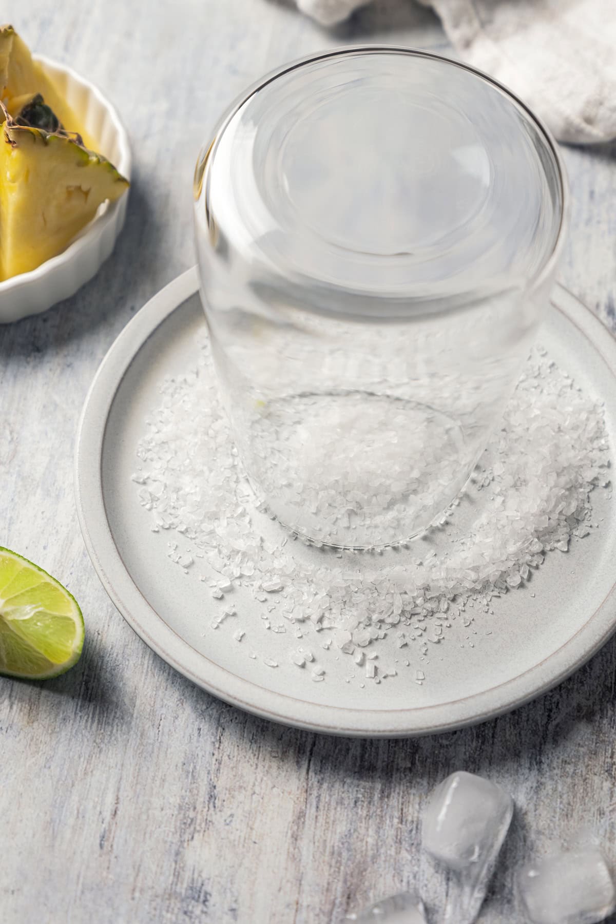 This easy pineapple margarita is a juicy blend of tequila blanco, fresh pineapple juice, and lime, shaken over ice. Don’t forget a salt rim! A glass inverted into a plate of salt, to make a salt rim.