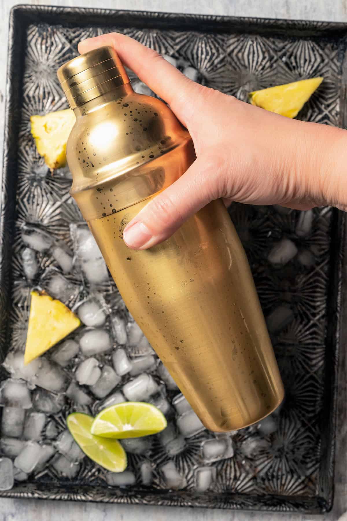 This easy pineapple margarita is a juicy blend of tequila blanco, fresh pineapple juice, and lime, shaken over ice. Don’t forget a salt rim! A hand shaking a pineapple margarita inside a golden cocktail shaker.