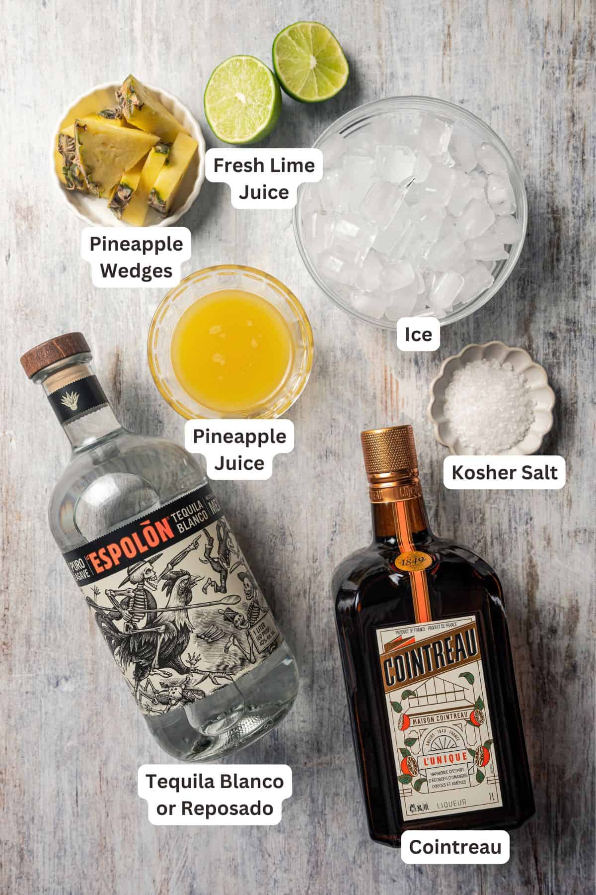 This easy pineapple margarita is a juicy blend of tequila blanco, fresh pineapple juice, and lime, shaken over ice. Don’t forget a salt rim! Pineapple margarita ingredients with text labels overlaying each ingredient.
