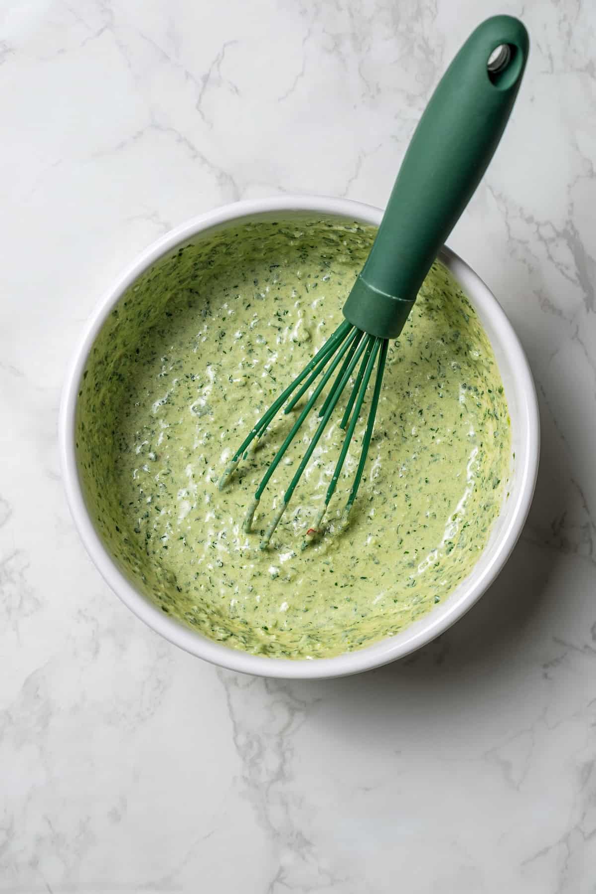 Creamy zhoug sauce in a bowl with a whisk.