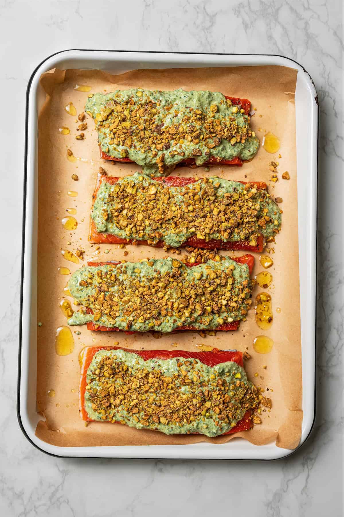 Salmon filets topped with creamy zhoug sauce and crushed pistachios on a parchment-lined baking sheet.