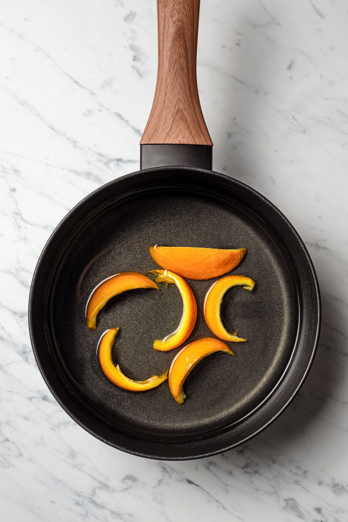 Orange rinds added to simple syrup ingredients in a cast iron skillet.