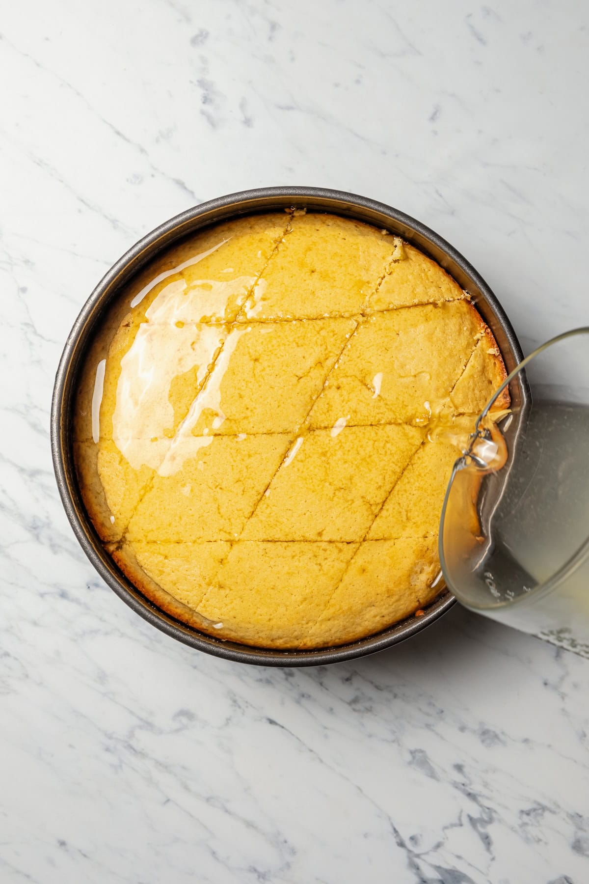 Pouring lemon-orange simple syrup over the semolina cake after cutting it into diamond-shaped slices.