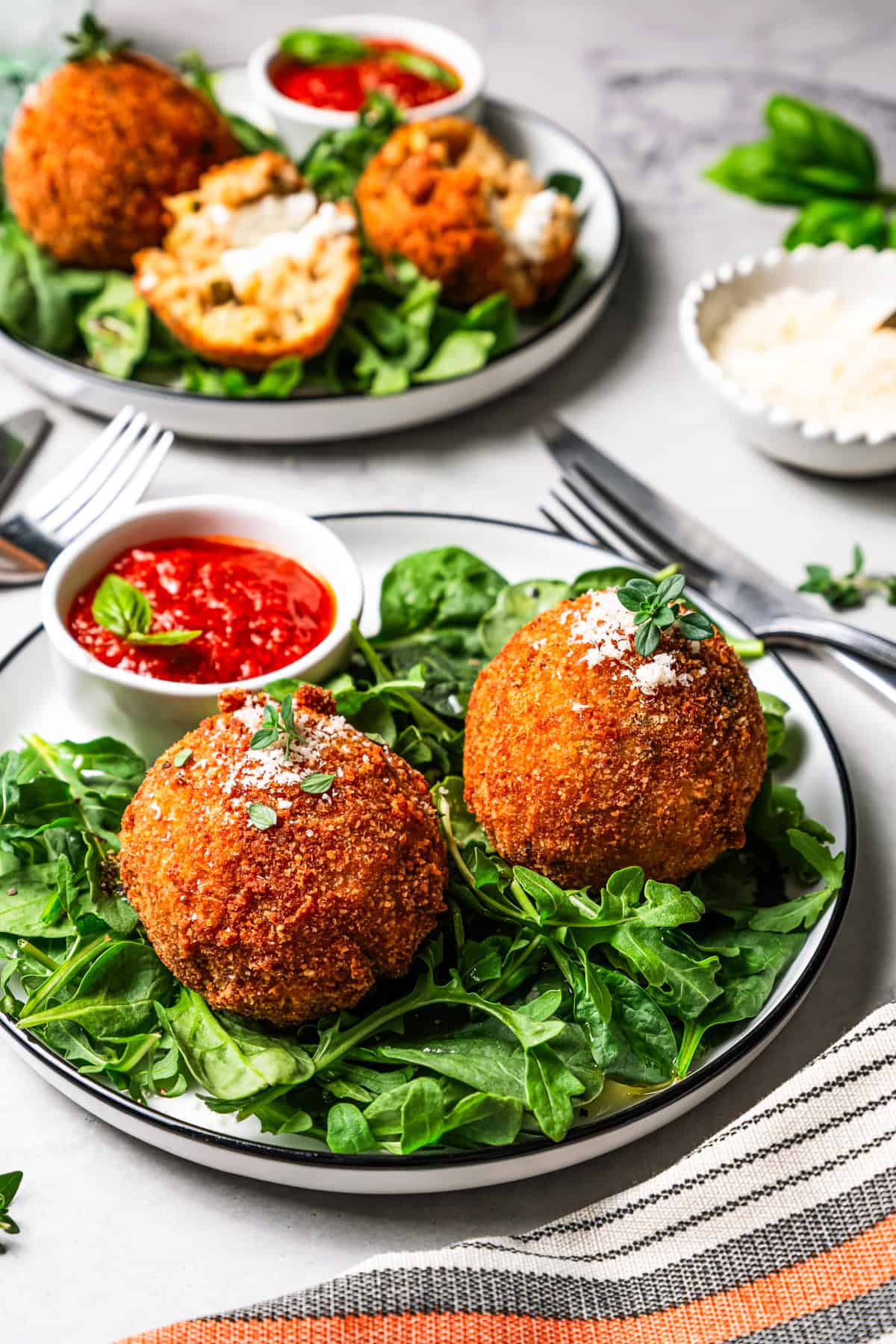This easy homemade arancini recipe makes crispy, cheesy, golden-fried Italian rice balls filled with melty pockets of tangy goat cheese. Two arancini set over salad greens on a plate.