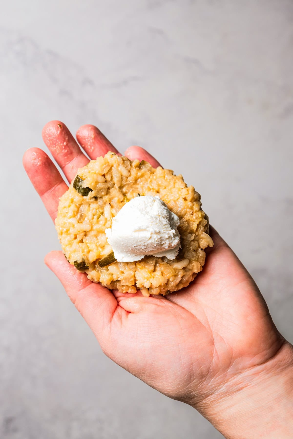 This easy homemade arancini recipe makes crispy, cheesy, golden-fried Italian rice balls filled with melty pockets of tangy goat cheese. A hand holding a ball of goat cheese set over flattened risotto.