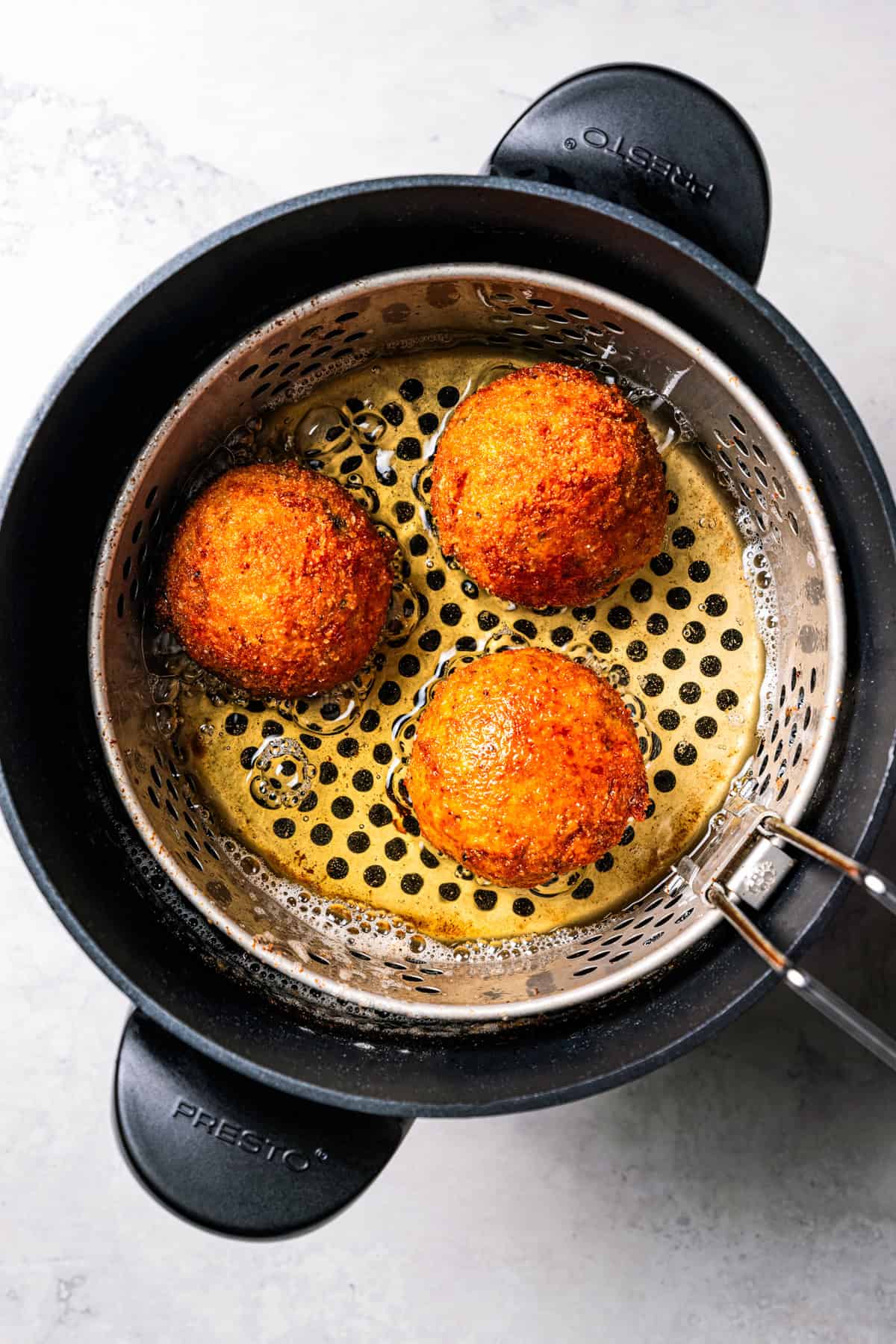 This easy homemade arancini recipe makes crispy, cheesy, golden-fried Italian rice balls filled with melty pockets of tangy goat cheese. Cooking arancini balls in a deep fryer.