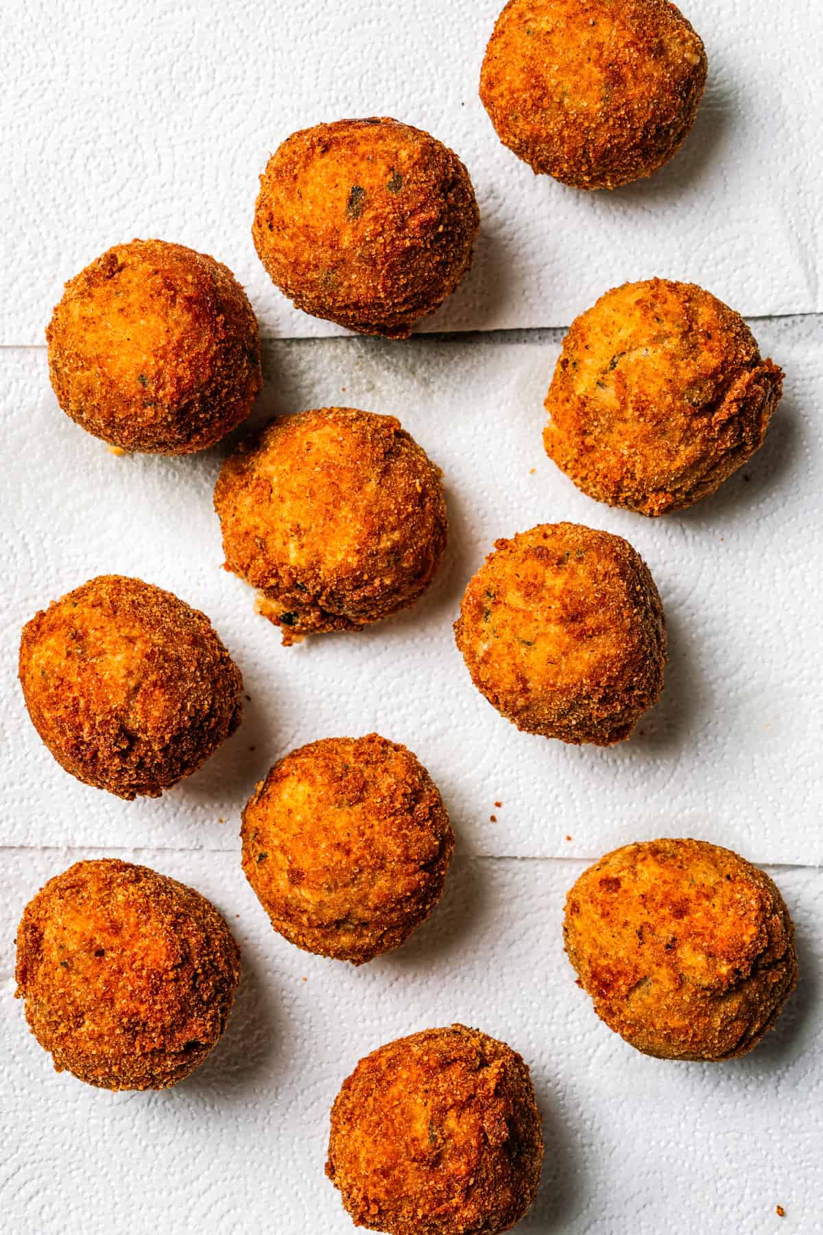 This easy homemade arancini recipe makes crispy, cheesy, golden-fried Italian rice balls filled with melty pockets of tangy goat cheese. Several fried arancini are arranged on a white backdrop.