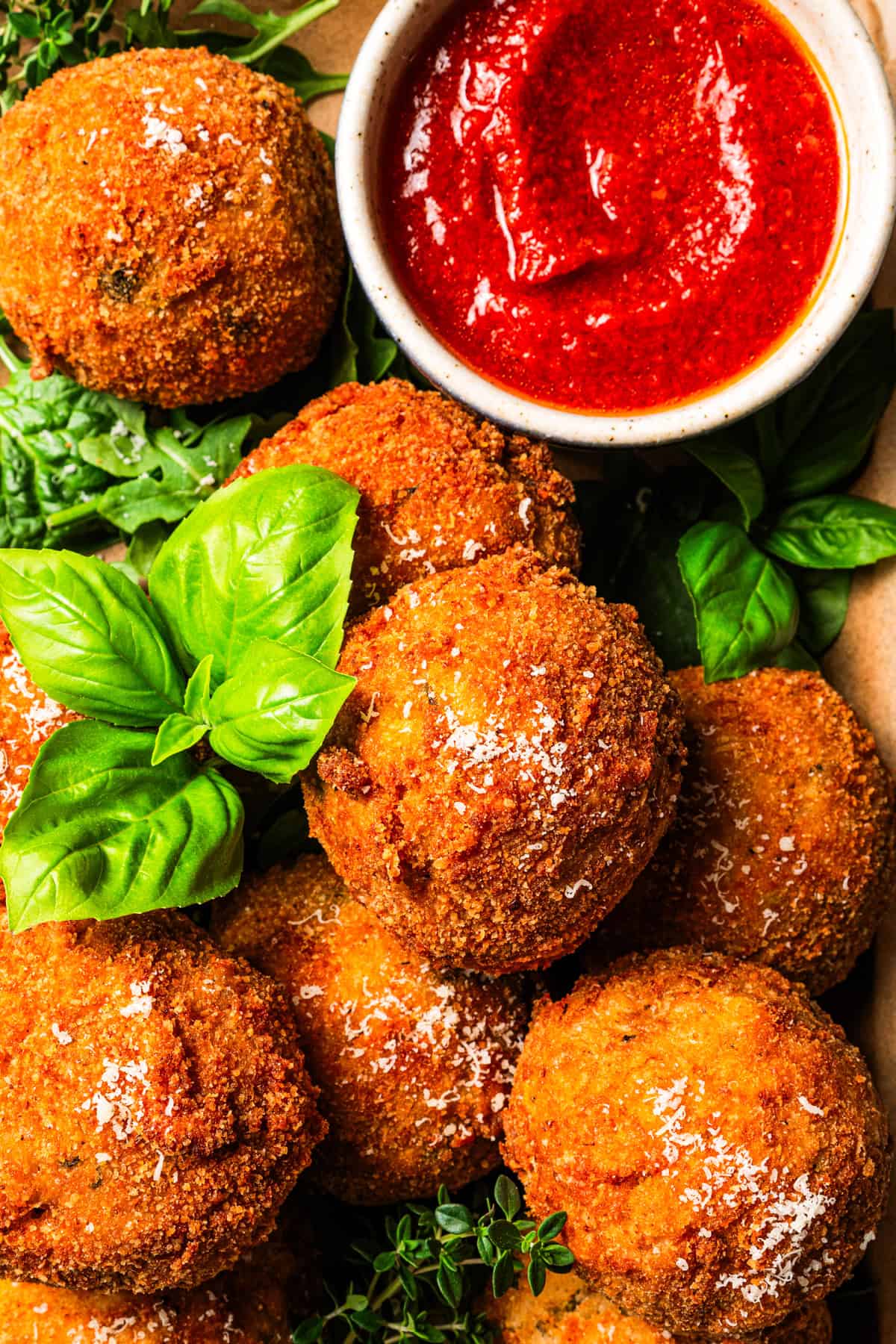 This easy homemade arancini recipe makes crispy, cheesy, golden-fried Italian rice balls filled with melty pockets of tangy goat cheese. Arancini are arranged on a tray with a bowl of marinara sauce to the side.