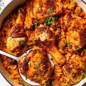 Overhead view of a serving spoon resting in a large pot of arroz con pollo.