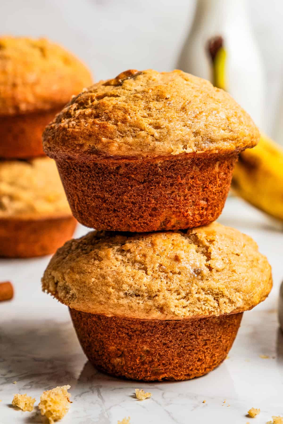 These soft, buttery banana bread muffins are easy to make with maple syrup, brown sugar, and cinnamon. It's impossible to eat just one! Two banana muffins stacked up.