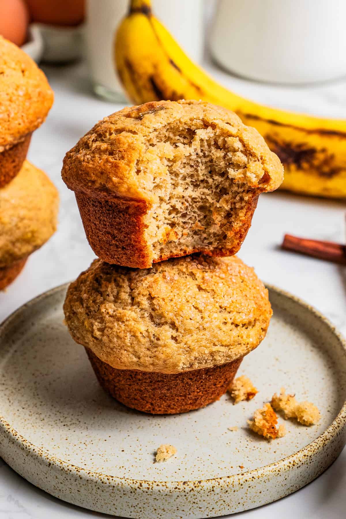 These soft, buttery banana bread muffins are easy to make with maple syrup, brown sugar, and cinnamon. It's impossible to eat just one! Two banana bread muffins stacked on a plate with a bite missing from the top muffin.