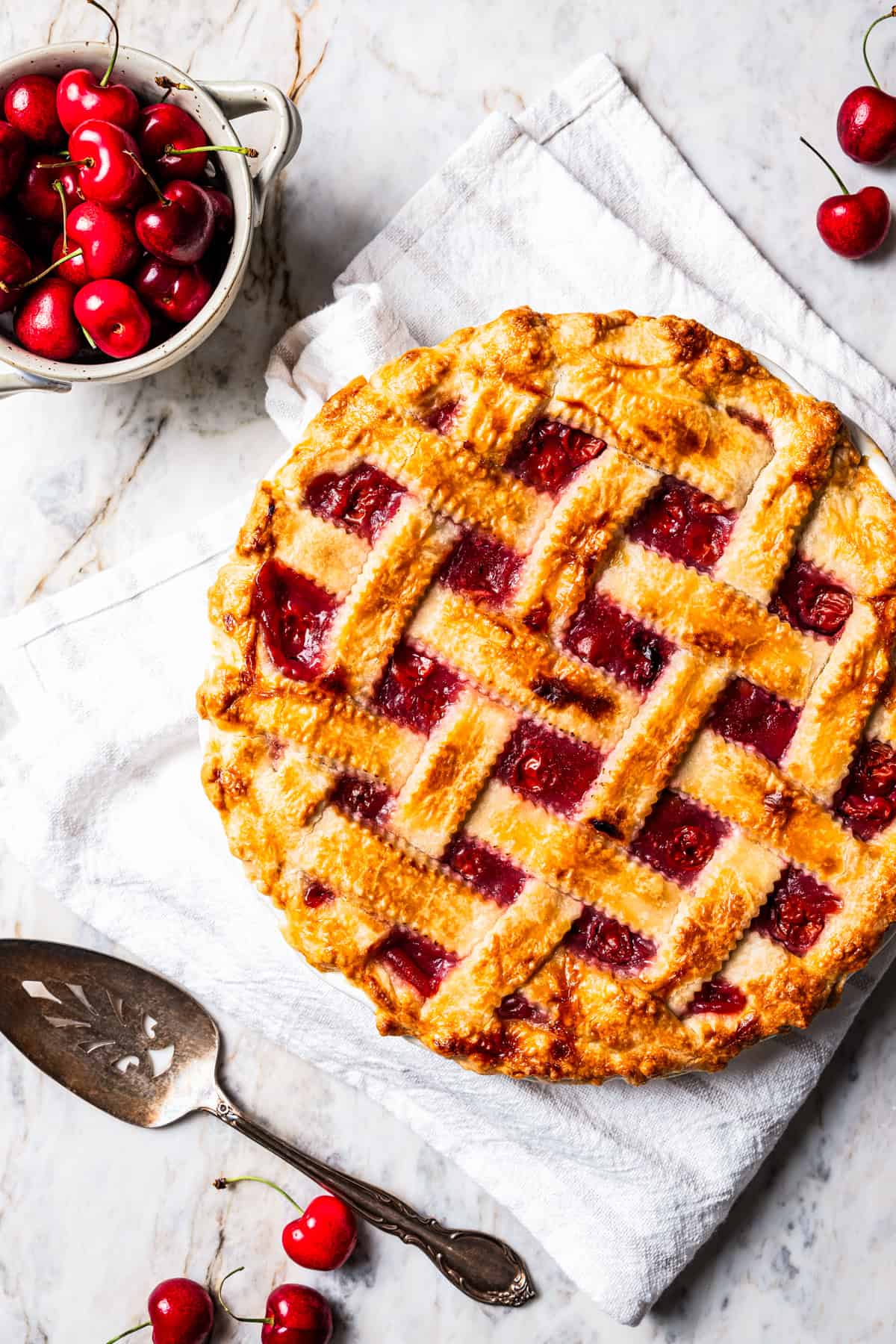 This is the best cherry pie recipe with thick, juicy cherry pie filling flavored with a touch of almond, baked in a buttery, flaky pie crust. Overhead view of a cherry pie with a lattice crust in a pie plate next to a bowl of cherries.
