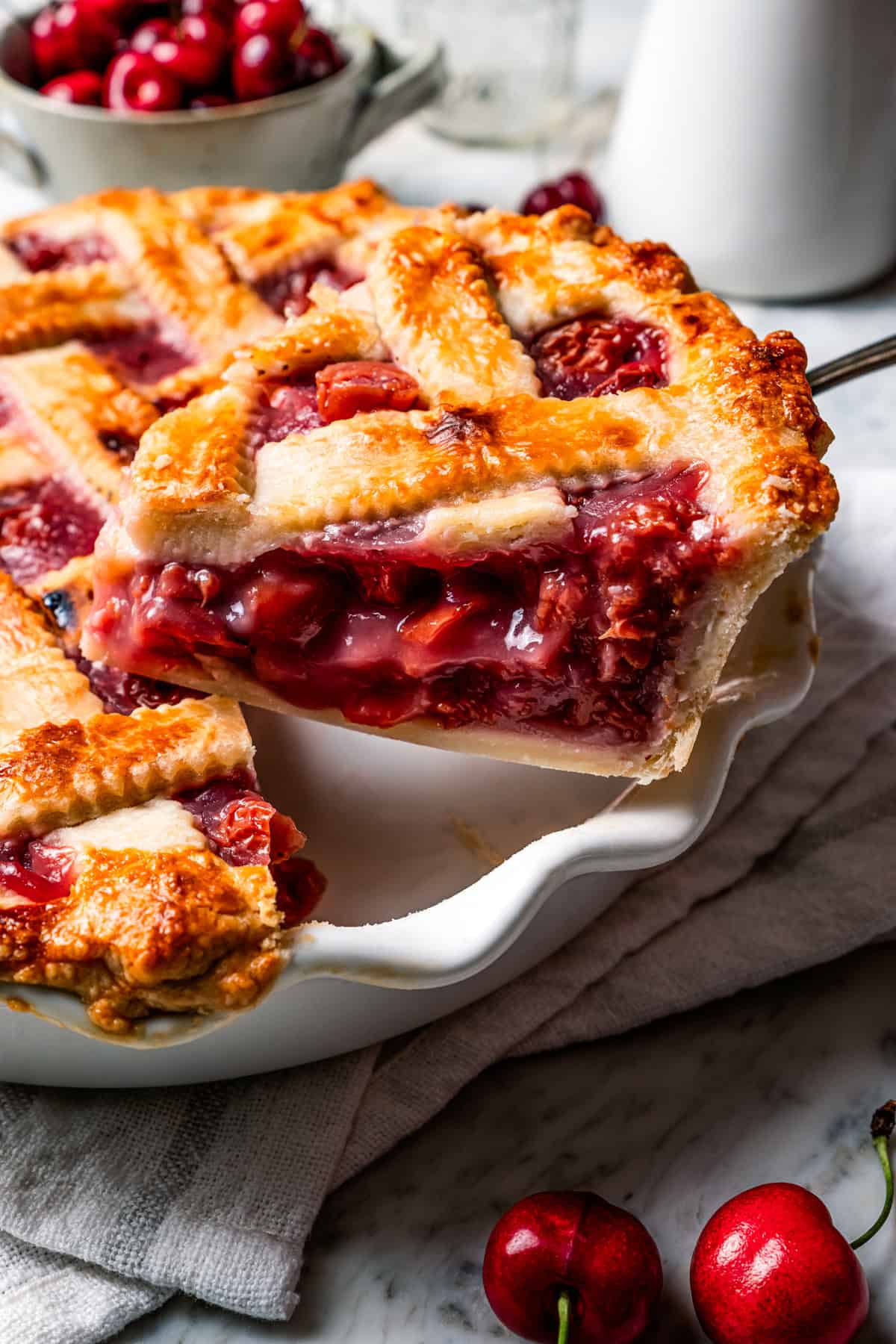 This is the best cherry pie recipe with thick, juicy cherry pie filling flavored with a touch of almond, baked in a buttery, flaky pie crust. A slice of cherry pie being lifted from the rest of the pie in a pie plate.