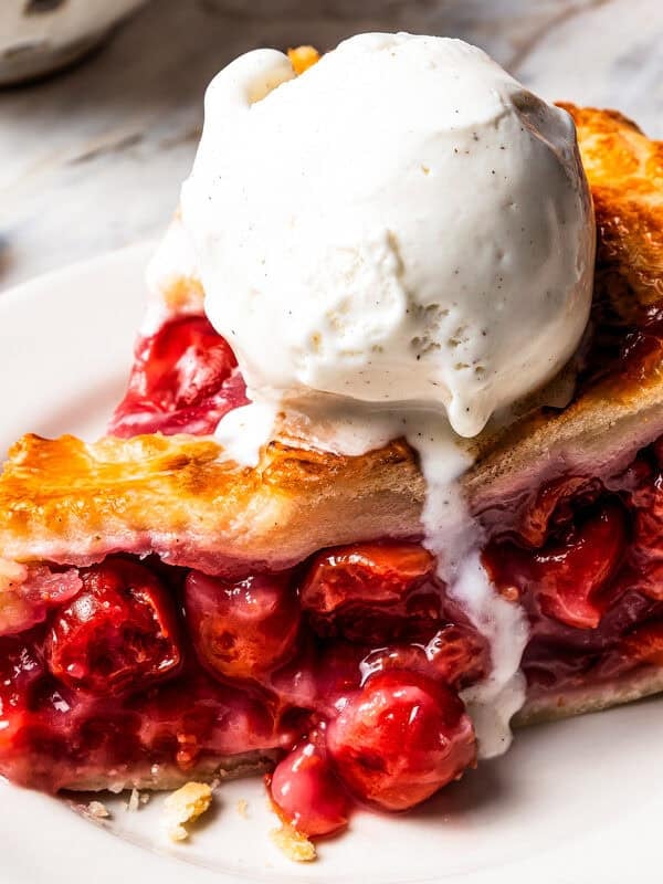 A slice of cherry pie served with a scoop of ice cream.
