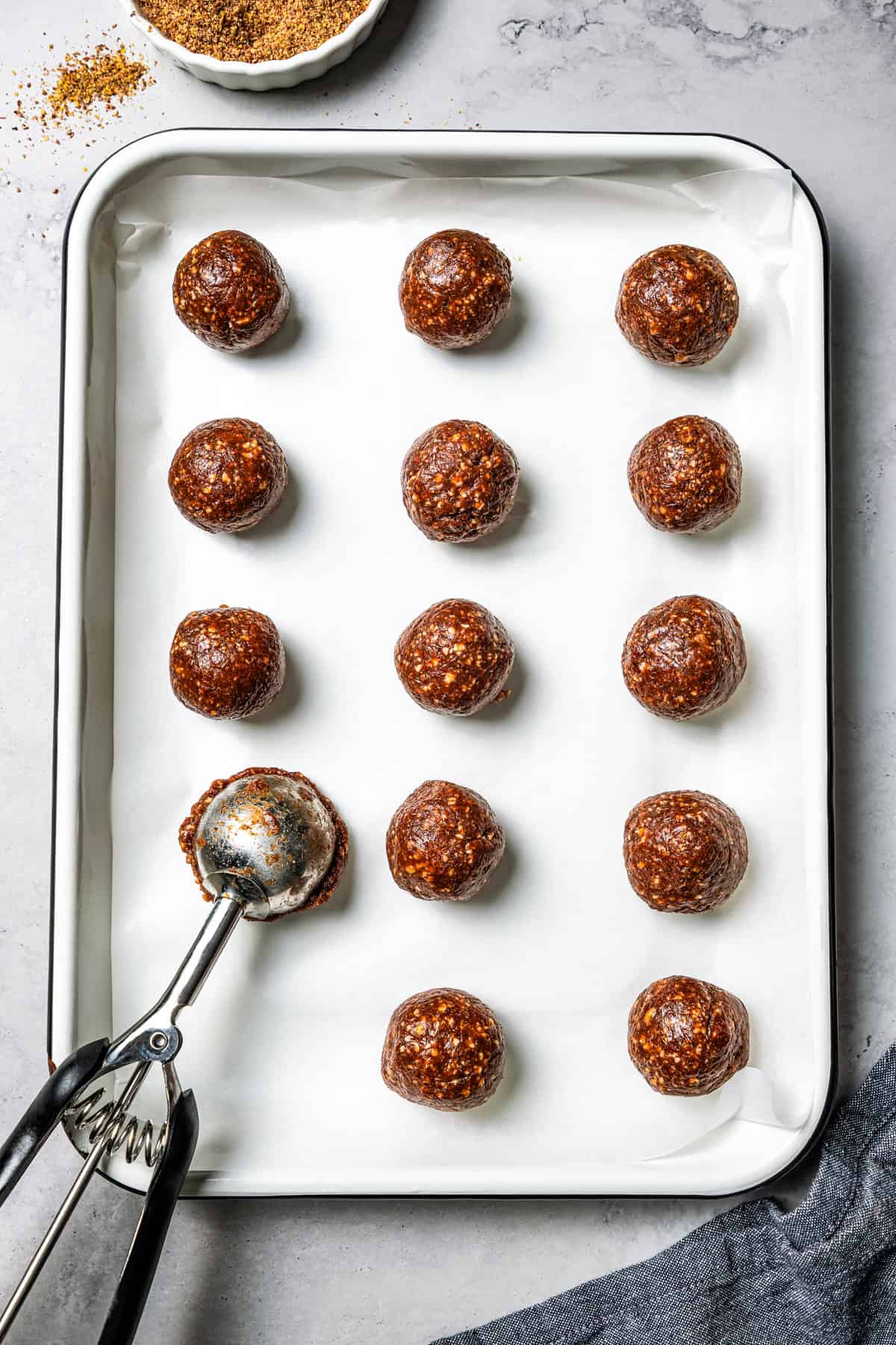 These easy no-bake energy balls are the perfect on-the-go snack packed with juicy dates, raw almonds, chocolate, and nut butter. No oats! A cookie scoop dropping energy balls onto a tray.