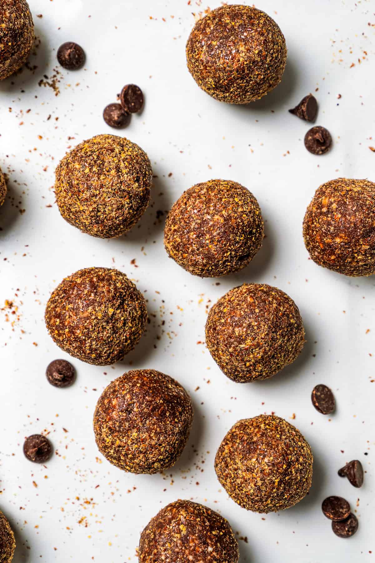 These easy no-bake energy balls are the perfect on-the-go snack packed with juicy dates, raw almonds, chocolate, and nut butter. No oats! Energy balls scattered on a countertop next to chocolate chips.