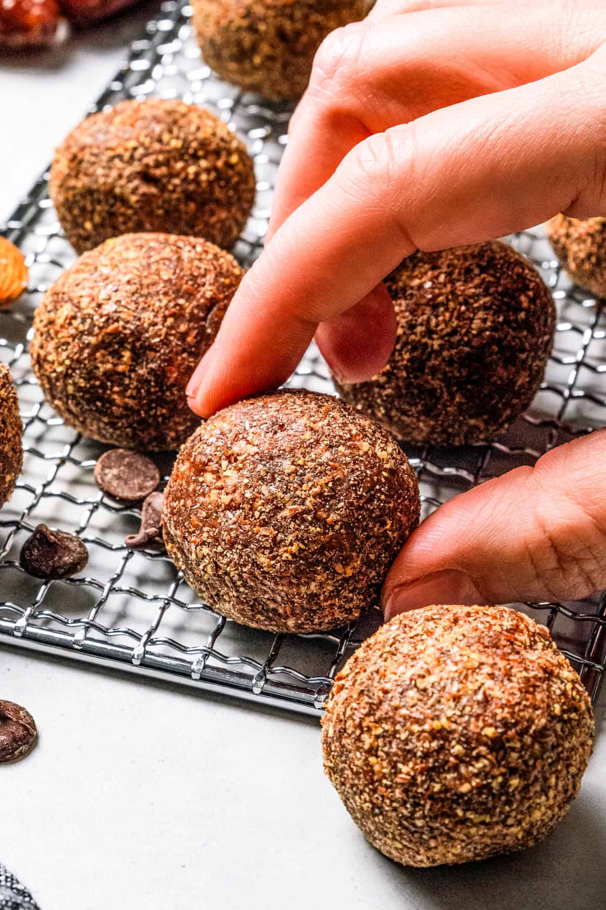 These easy no-bake energy balls are the perfect on-the-go snack packed with juicy dates, raw almonds, chocolate, and nut butter. No oats! A hand picking up an energy ball from a wire rack, surrounded by more energy balls.