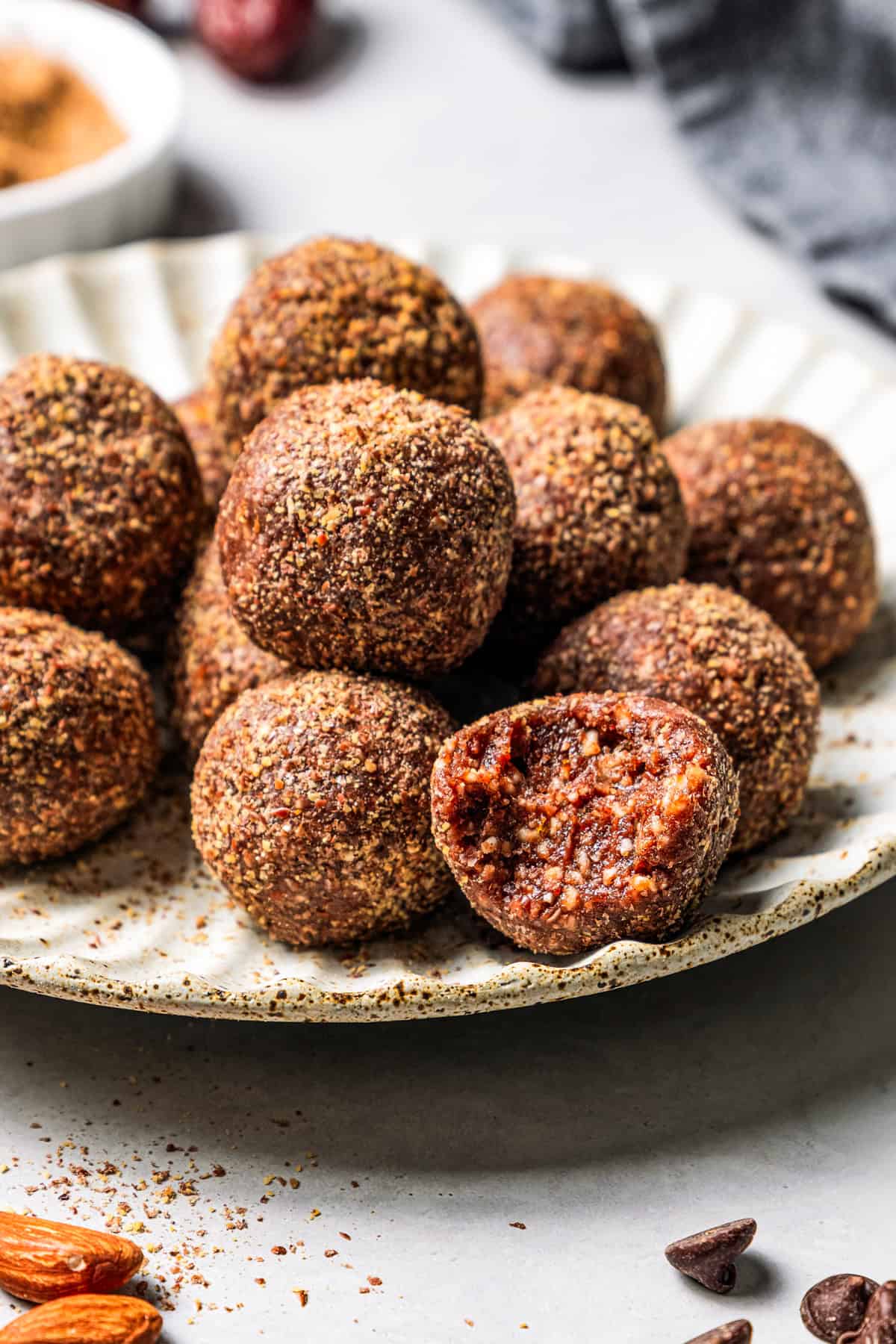 These easy no-bake energy balls are the perfect on-the-go snack packed with juicy dates, raw almonds, chocolate, and nut butter. No oats! Energy balls on a plate with a bite missing from one ball.