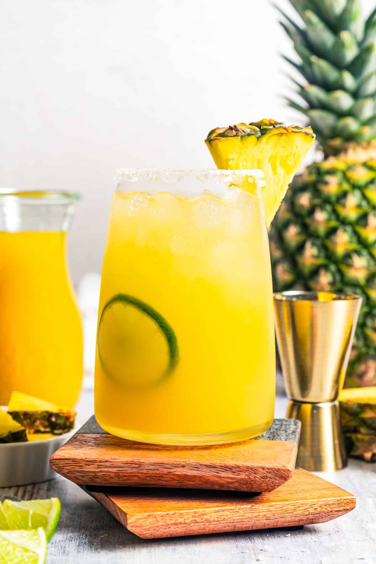 This easy pineapple margarita is a juicy blend of tequila blanco, fresh pineapple juice, and lime, shaken over ice. Don’t forget a salt rim! Margarita in a salt-rimmed glass garnished with a pineapple wedge and lime slice, with a second margarita in the background.