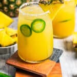 Pineapple margaritas served in drinking glasses with a garnish of jalapeno slices and pineapple wedges.